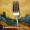 A fork is on top of a painting looking out across the countryside